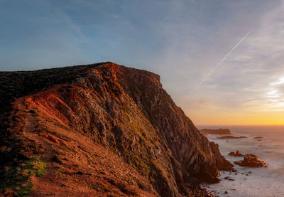 Rock formation on beach against sky during sunset