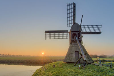 Traditional windmill on field against clear sky during sunset
