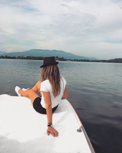 Rear view of woman sitting on white boat over lake against sky