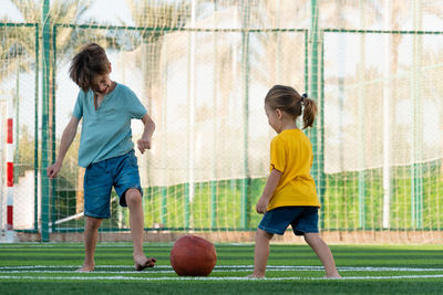 Boy and girl playing football on green sports field.