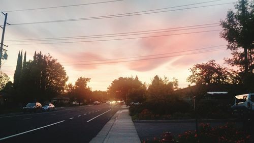 Road by trees against sky during sunset