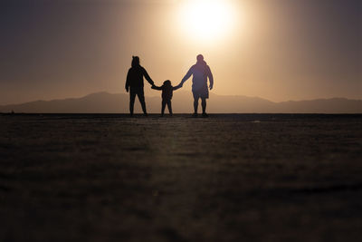 Silhouette friends standing on beach against sky during sunset