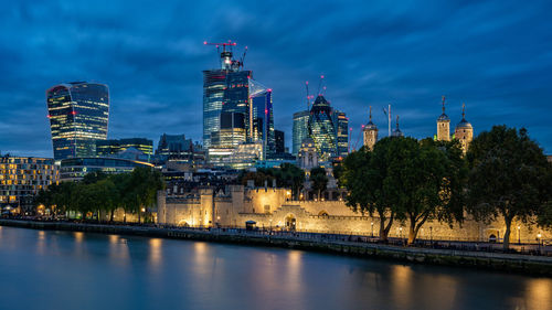 Illuminated buildings by river against sky in city