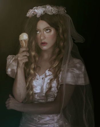 Thoughtful female model in costume having ice cream cone against black background