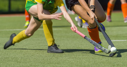 Low section of female players playing hockey on field