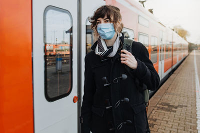 Woman wearing mask standing by train on railroad station platform