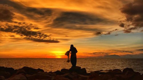 Woman standing on rock by sea against sky during sunset