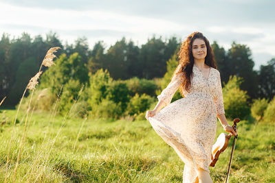 Portrait of young attractive woman standing with violin on the grassy field