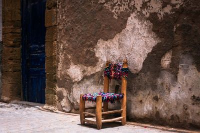 Empty wooden chair by weathered wall