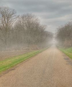 Road amidst bare trees against sky