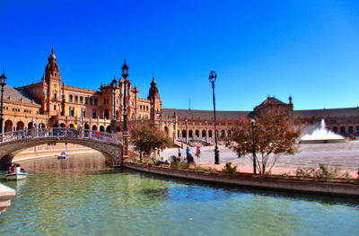 Arch bridge over canal and buildings against clear blue sky