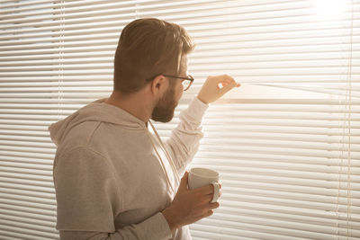 Midsection of man holding coffee while standing by window
