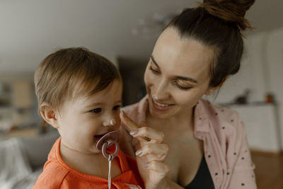 Smiling mother applying cream on nose of daughter at home