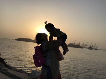 Rear view of woman standing at beach during sunset with her daughter 