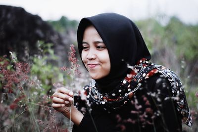 Close-up of smiling woman wearing hijab looking at plant