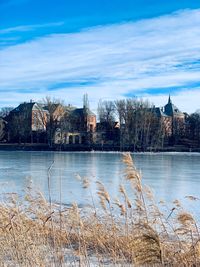 View of buildings by lake against cloudy sky