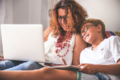 Young woman using phone while sitting on laptop