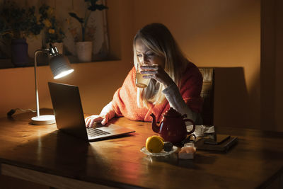 Woman using phone while sitting on table at home