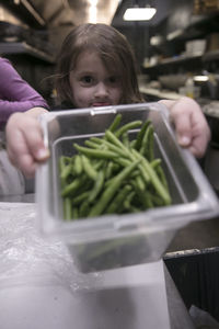 Girl holding green beans in container in kitchen