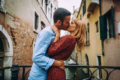 Young couple kissing while standing on bridge in city