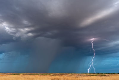 Lightning over field against storm clouds