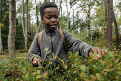 Curious boy picking berries from plants in forest during vacation