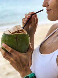 Midsection of woman drinking coconut water at beach