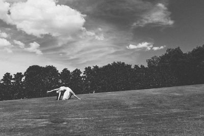 Full length of woman stretching on field against cloudy sky