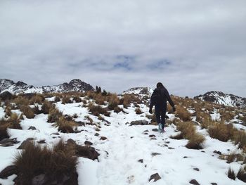 Rear view of hiker hiking on snow covered mountain against cloudy sky