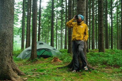 Young man having drink while camping in forest