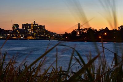 Silhouette buildings by river against sky at sunset