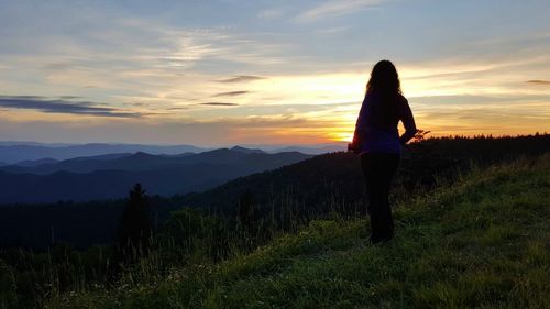 Rear view full length of woman standing against mountains during sunset