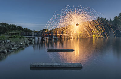 Illuminated ferris wheel by lake against sky at night