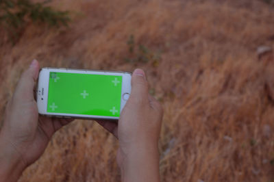 Cropped hands of person holding smart phone against dry grass