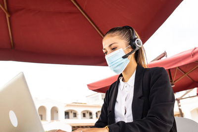 Woman wearing mask working on laptop outdoors