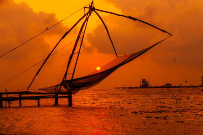 Silhouette of fishing net in sea against orange sky