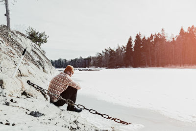 Side view of mid adult man sitting on snow covered field against sky