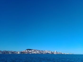 Sea by buildings against clear blue sky