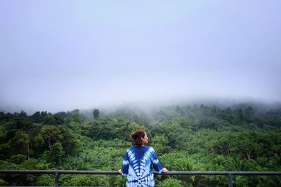 Rear view of woman standing by trees in forest against clear sky