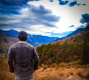 Rear view of man looking at mountains against sky