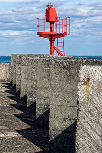 Lighthouse by concrete wall against sky