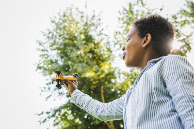 Young woman holding violin while standing against sky