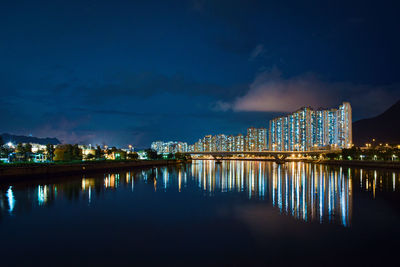 Illuminated buildings by lake against sky at night