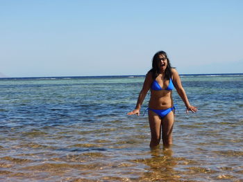 Full length of young woman standing in sea against clear sky