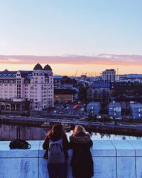 Rear view of woman standing by buildings against sky during sunset