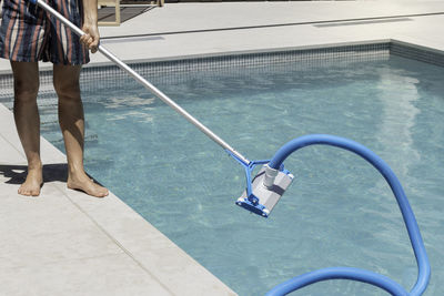 Unrecognizable man cleaning the swimming pool with an automatic pool cleaner at his house backyard