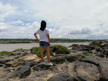 Rear view of man standing on rock against sky