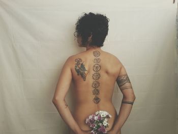 Rear view of shirtless young woman with tattoo on back