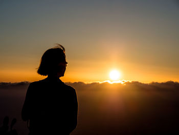 Silhouette woman standing against orange sky during sunset