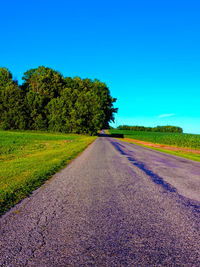 Empty road along trees on field